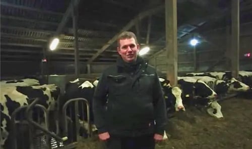 Landwirt Jens Thiessen steht zufrieden in seinem modernen Stall bei einer Holstein-Kuh, deren Laktationsstart durch den PerformaNat CalciumBolus sicher begleitet wird.