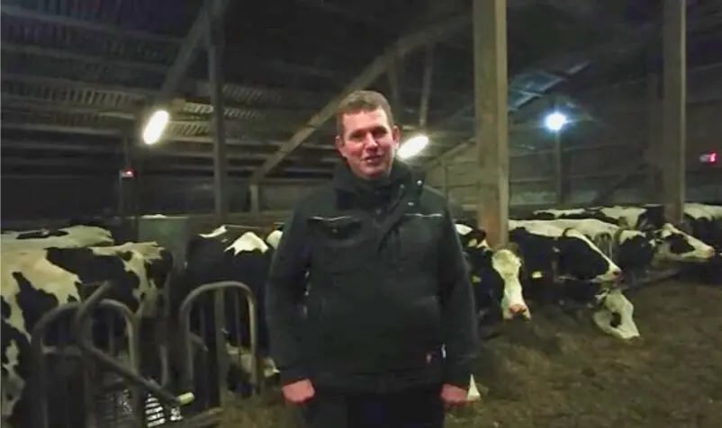 Landwirt Jens Thiessen steht zufrieden in seinem modernen Stall bei einer Holstein-Kuh, deren Laktationsstart durch den PerformaNat CalciumBolus sicher begleitet wird.