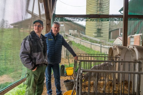 Ein Mitarbeiter von PerformaNat im fachlichen Austausch mit Michael Rentschler. Sie stehen unter einem Vordach neben Kälberiglus mit Stroheinstreu, in denen ein junges Kalb zu sehen ist. Im Hintergrund erstrecken sich das grüne Hofgelände, Wirtschaftsgebäude und ein Futtersilo.