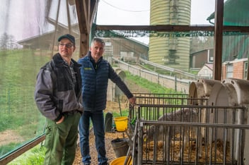 Ein Mitarbeiter von PerformaNat im fachlichen Austausch mit Michael Rentschler. Sie stehen unter einem Vordach neben Kälberiglus mit Stroheinstreu, in denen ein junges Kalb zu sehen ist. Im Hintergrund erstrecken sich das grüne Hofgelände, Wirtschaftsgebäude und ein Futtersilo.