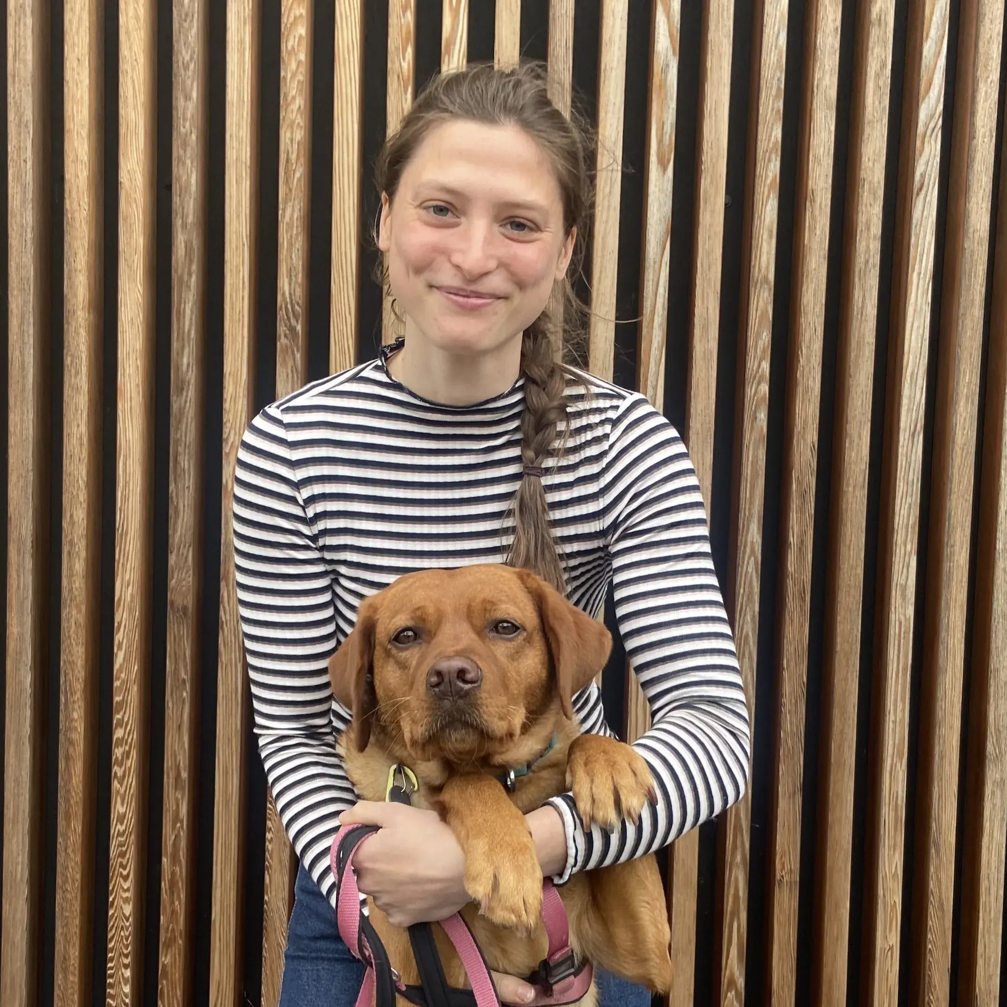 Nina Wagner lächelt mit ihrem Hund im Arm in die Kamera. Sie ist bei PerformaNat in der Kundenbetreuung tätig.
