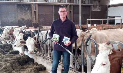 Ein Foto von einem Mann, der vor seinen Kühen steht und das Calcium Bolus Produkt von PerformaNat in der Hand hält