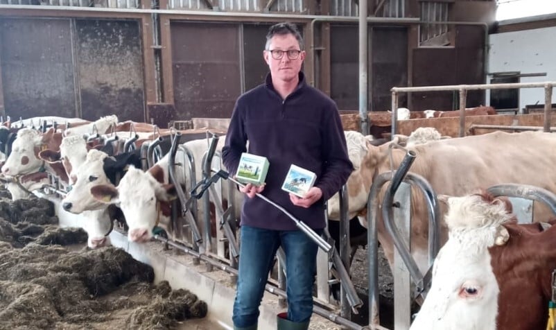 Ein Foto von einem Mann, der vor seinen Kühen steht und das Calcium Bolus Produkt von PerformaNat in der Hand hält
