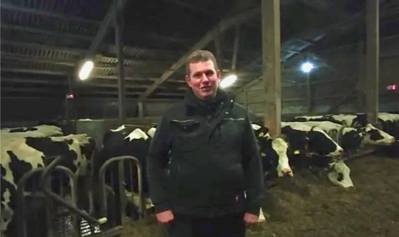 Landwirt Jens Thiessen steht zufrieden in seinem modernen Stall bei einer Holstein-Kuh, deren Laktationsstart durch den PerformaNat CalciumBolus sicher begleitet wird.